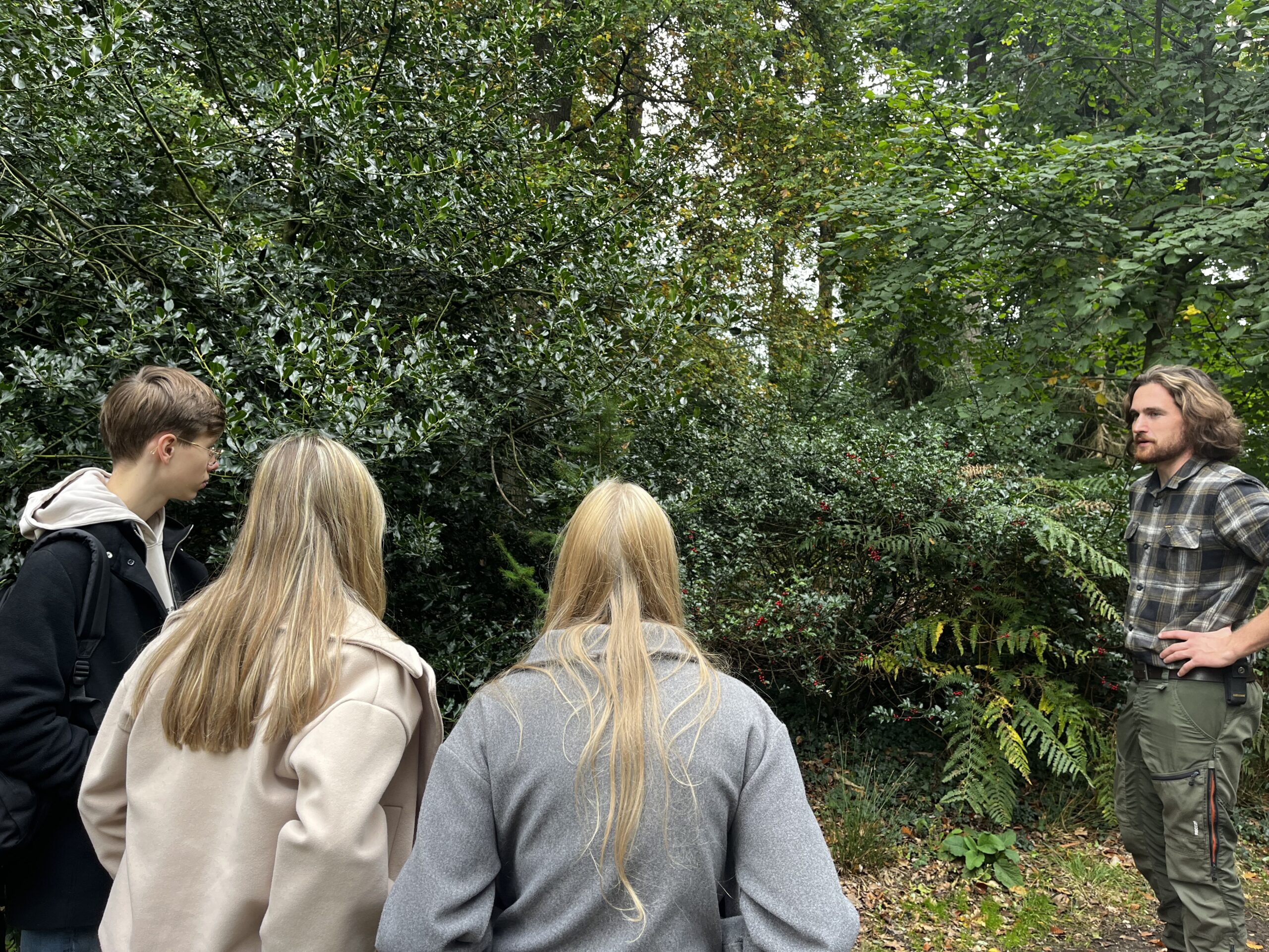 Groep mensen luistert aandachtig naar gids in een groen bos.