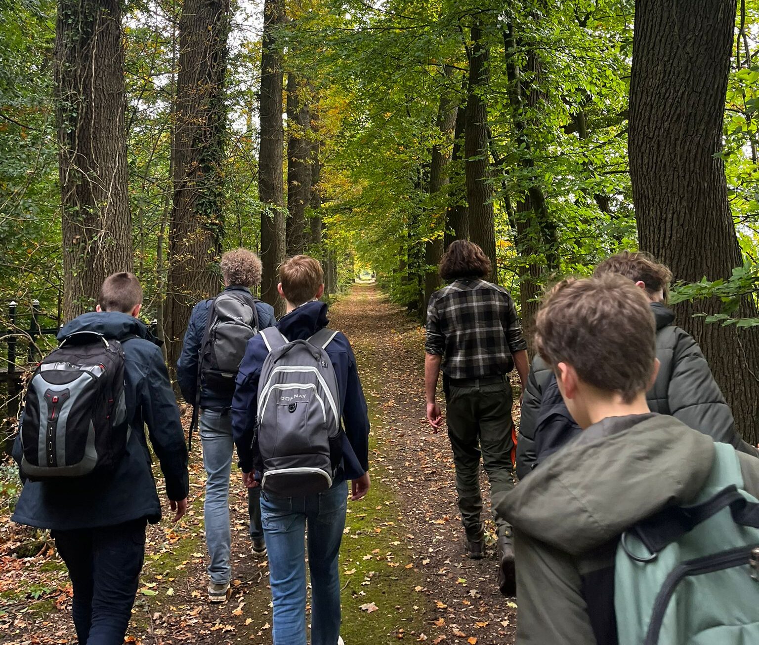 Groep jongeren wandelt door een groen bos over een met bladeren bedekt pad.