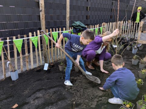 Twee kinderen en een volwassene planten een boom in een tuin.