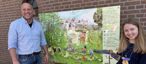 Man en meisje poseren naast een natuureducatiebord over lente, tegen een bakstenen muur.