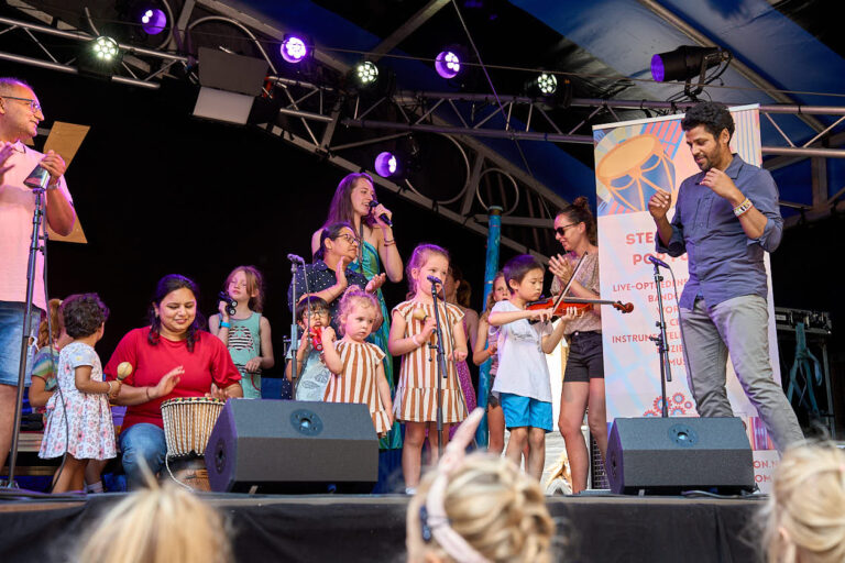 Groep mensen op een podium, kinderen spelen muziekinstrumenten voor publiek.