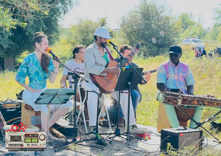 Muziekgroep speelt buiten op zonnige dag, met gitaren en percussie-instrumenten.