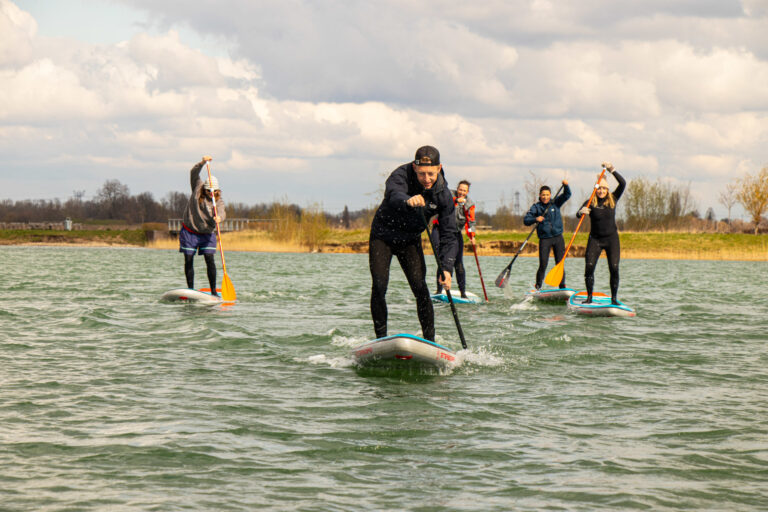 Groep mensen paddleboarden op een meer onder een bewolkte hemel.