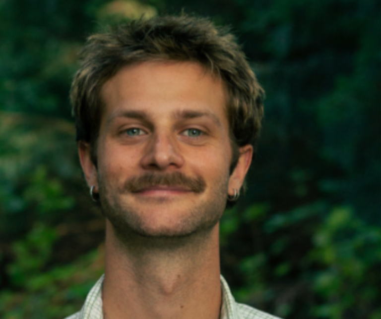Man met baard in een groene, bosachtige omgeving.