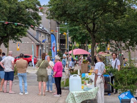 Buurtfeest op straat met kraampjes, mensen in gesprek en kleurrijke vlaggetjes.