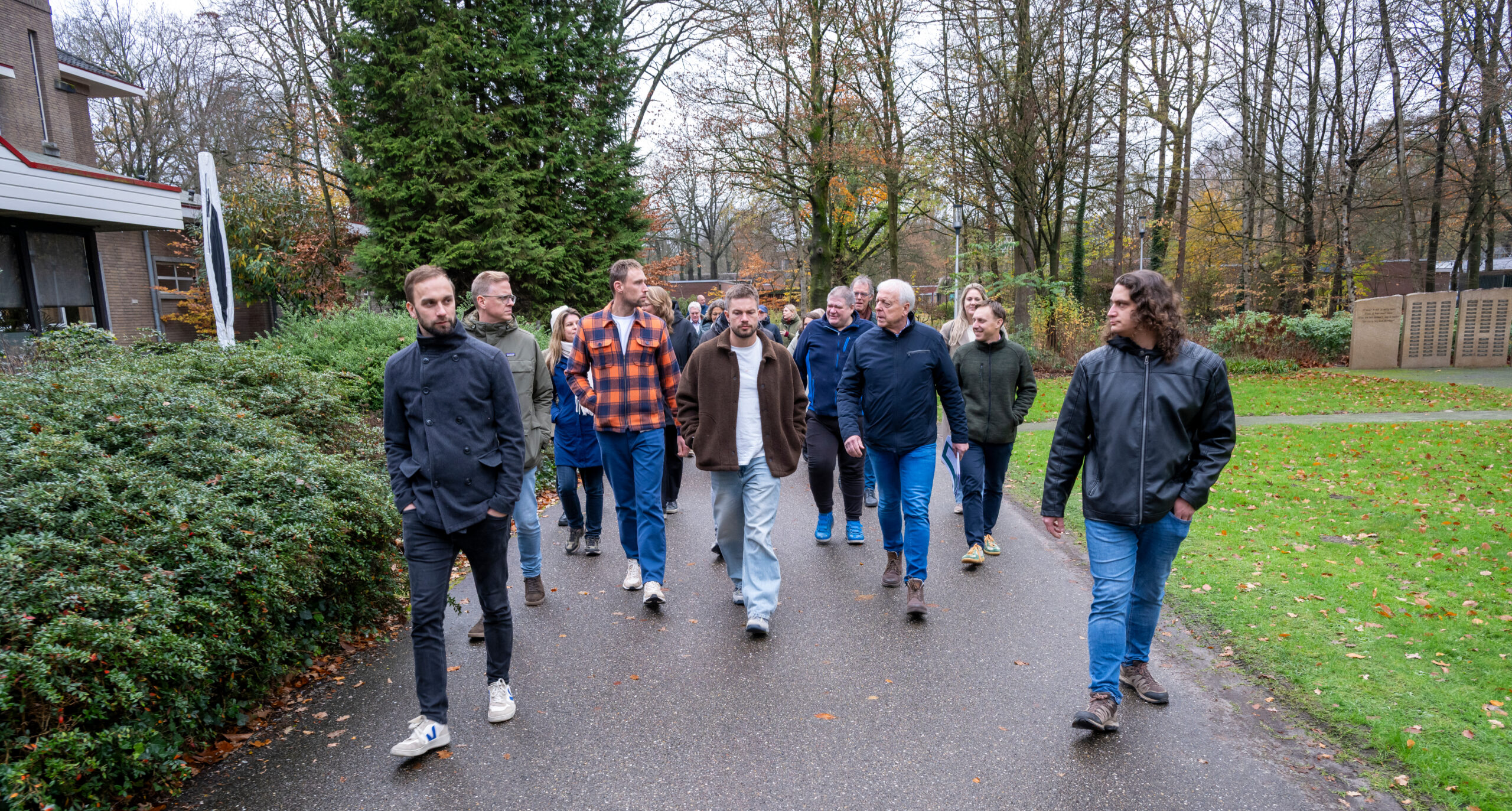 Een groep mensen loopt buiten op een parkpad in een herfstlandschap.