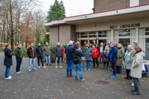 Groep mensen staat bijeen voor gebouw Het Vierhuis op een herfstige dag.
