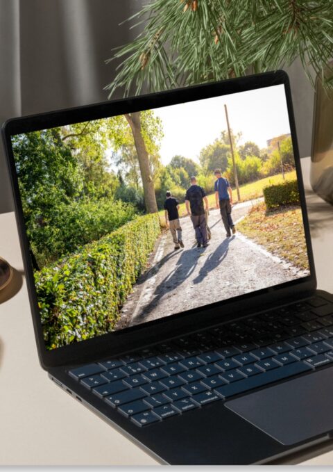 Drie mensen wandelen op zonnige dag op een pad, foto weergegeven op een laptop.