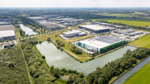 Luchtfoto van een industriegebied met magazijnen omringd door waterwegen en groen landschap.