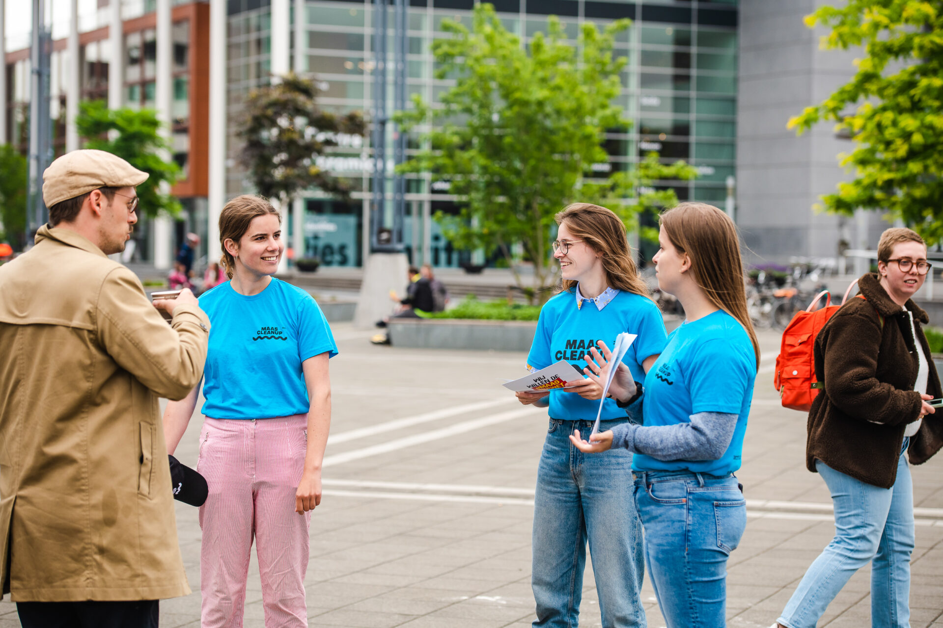 Mensen in blauwe shirts hebben een gesprek buiten in een stedelijke omgeving met bomen en een gebouw.
