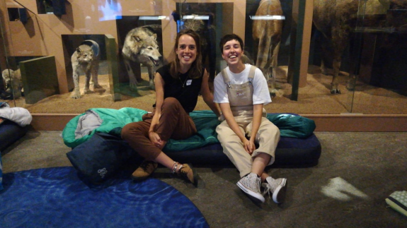 Twee mensen zitten op kussens in een museum, met opgezette dieren op de achtergrond.