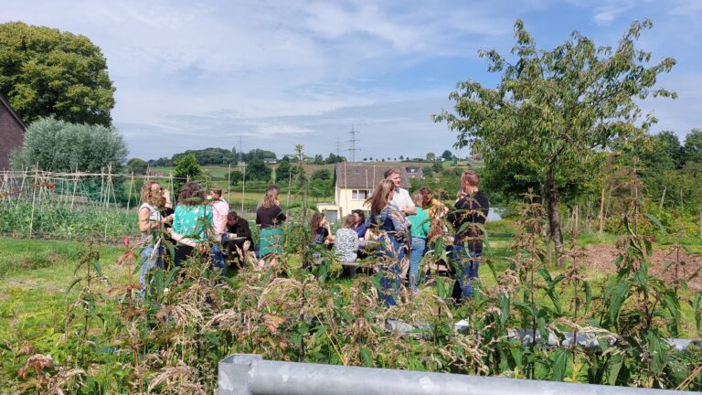 Groep mensen verzameld in een groene, landelijke tuin met bomen en een moestuin.