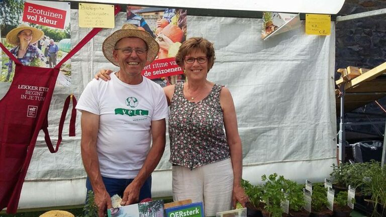 Twee mensen staan lachend bij een kraam met planten en informatieposters.