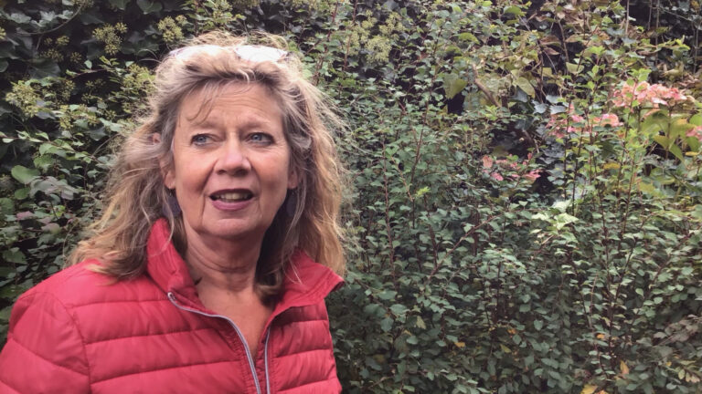 Een vrouw in een rode jas staat voor groen bladerdek.