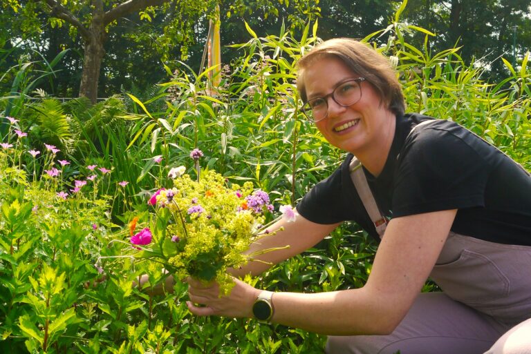 Vrouw knielt in tuin en plukt boeket kleurrijke bloemen met groene achtergrond.