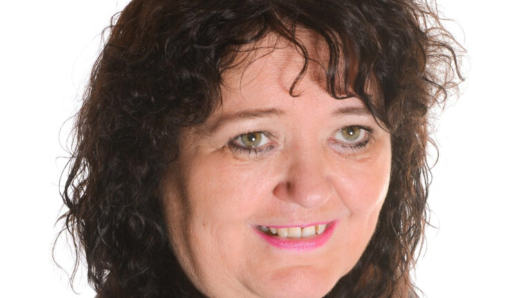 Vrouw met donker krullend haar en roze lippenstift lacht tegen een witte achtergrond.