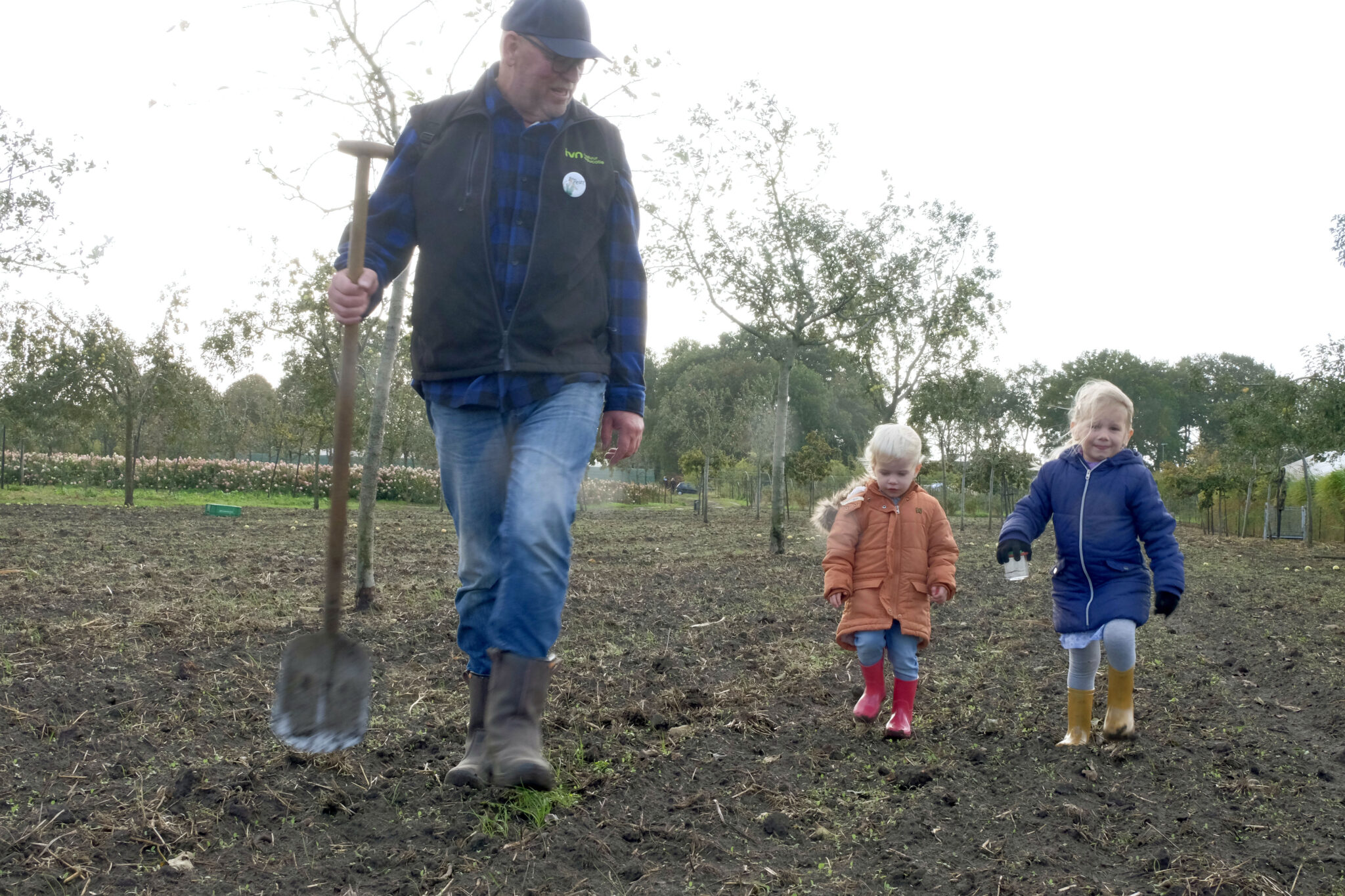 Kinderen lopen over erf met man met schep