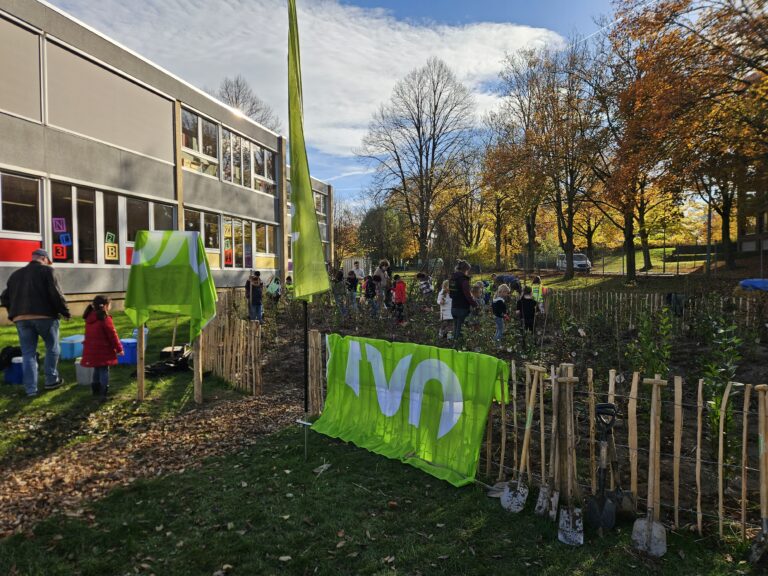 Mensen planten bomen in een tuin bij een schoolgebouw op een zonnige herfstdag.