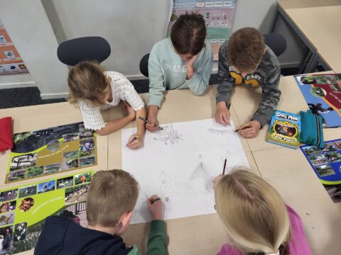 Vijf kinderen tekenen samen op papier met posters en een stripboek op tafel.