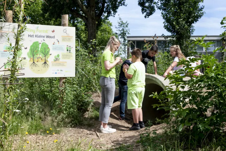Kinderen verkennen groene omgeving bij een bord met tekst 