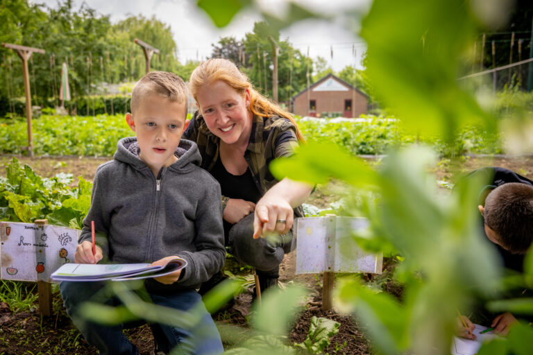 Een jongen leert met een vrouw in een tuin met planten.