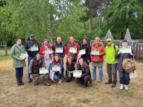 Een groep mensen poseert buiten met certificaten voor een bosrijke achtergrond.