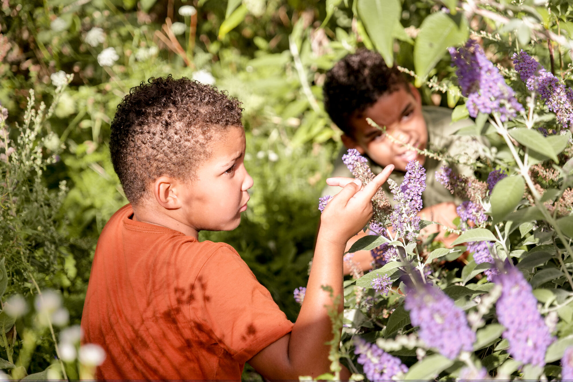 Twee kinderen bekijken paarse bloemen in een weelderige, groene tuin.