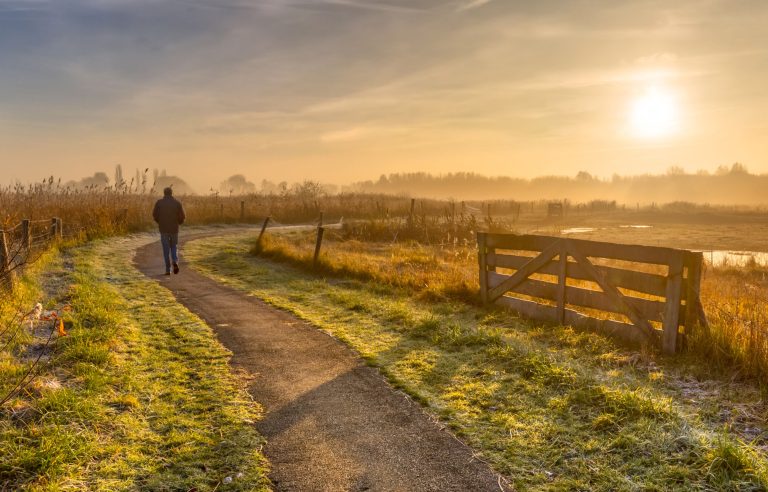 Wandelaar in weids landschap met laagstaande zon