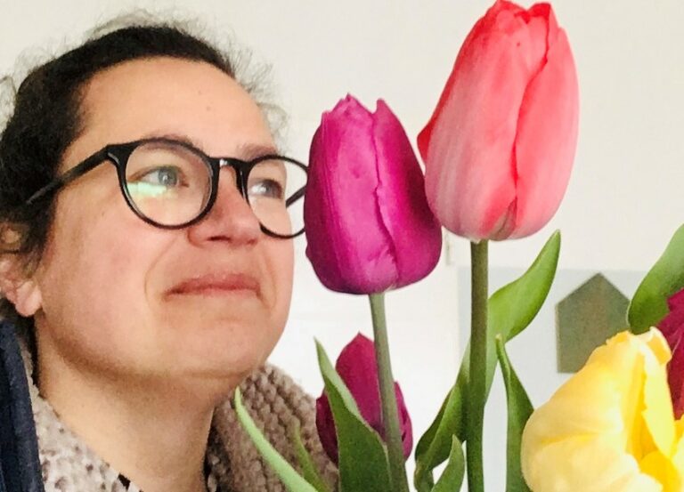 Vrouw met bril kijkt naar kleurrijke tulpen van dichtbij.