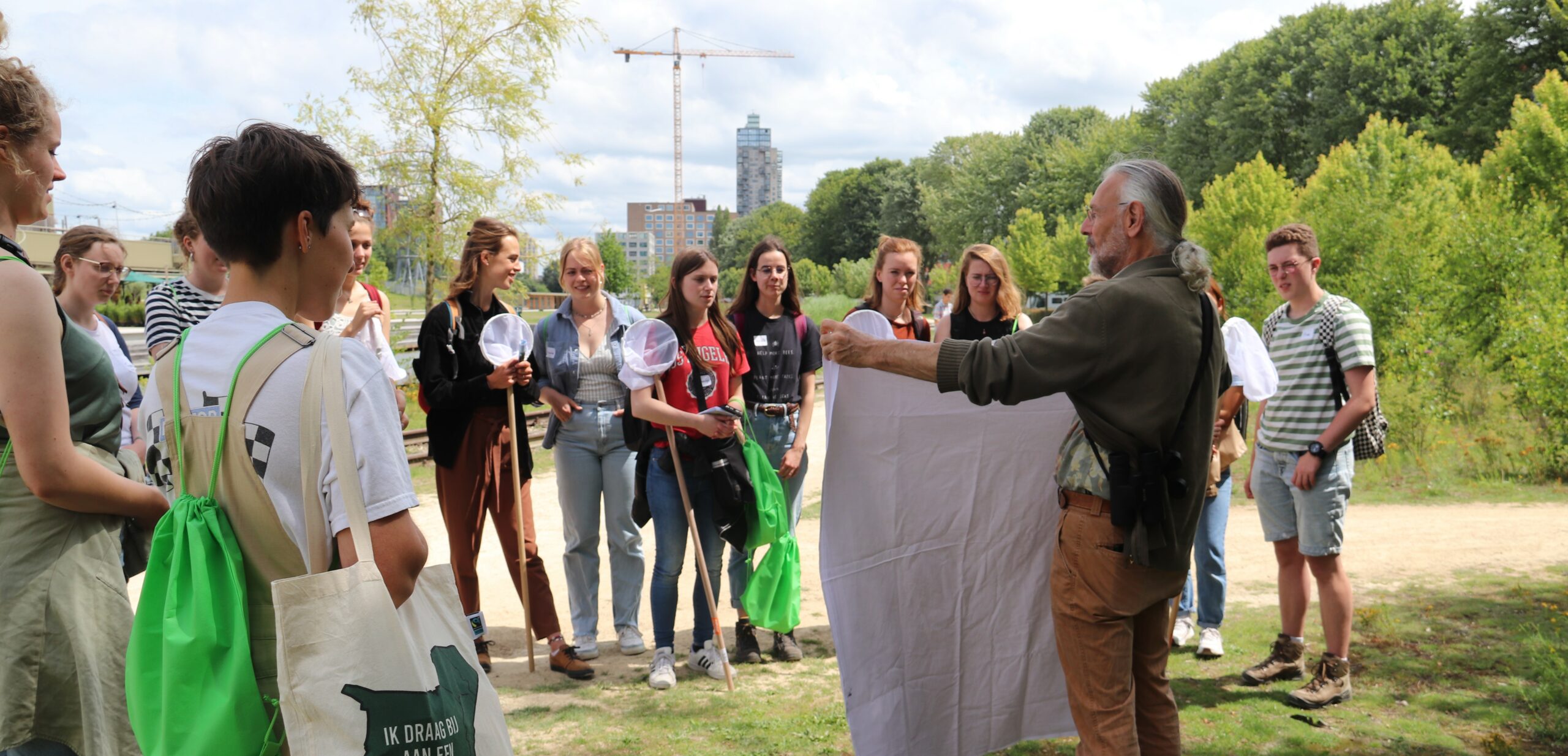 Een groep mensen volgt een buitenles, geleid door een man met een wit doek.