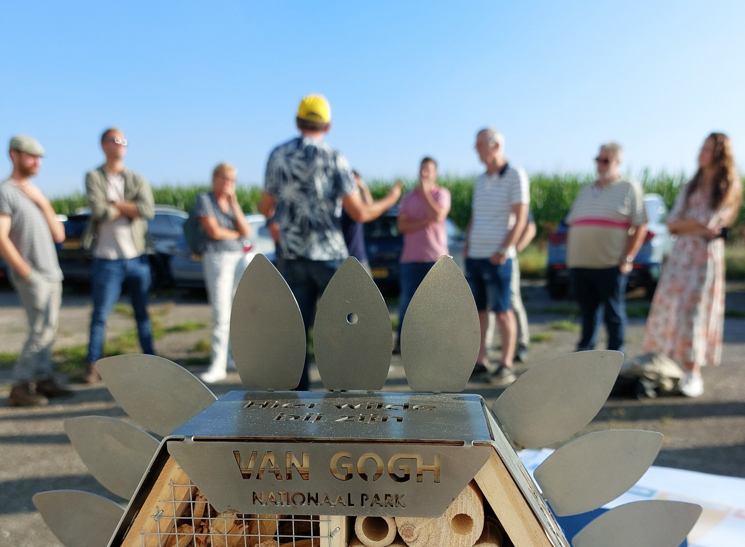 Metaal kunstwerk met tekst "Van Gogh Nationaal Park", mensen op achtergrond buiten.