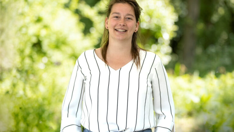 Vrouw in gestreepte blouse lacht buiten in een groene, wazige omgeving.