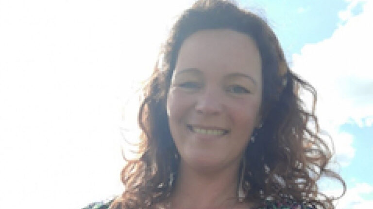 Een glimlachende vrouw met krullend haar buiten tegen een heldere hemel.