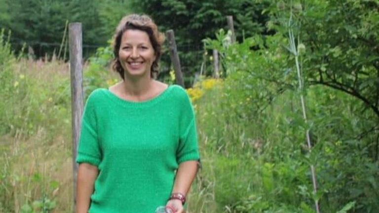 Vrouw in groene trui glimlacht in een weelderig, groen bosachtig gebied.