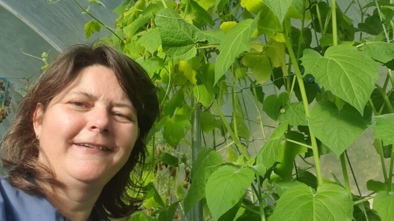 Vrouw in kas met groene planten en bladeren op de achtergrond.