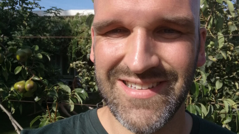 Glimlachende man in de zon met bomen en onrijpe peren op de achtergrond.