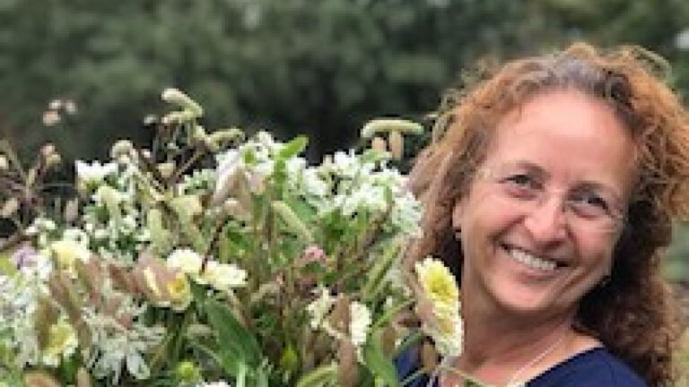 Vrouw met krullend haar glimlacht, houdt groot boeket witte bloemen vast. Bosachtige achtergrond.