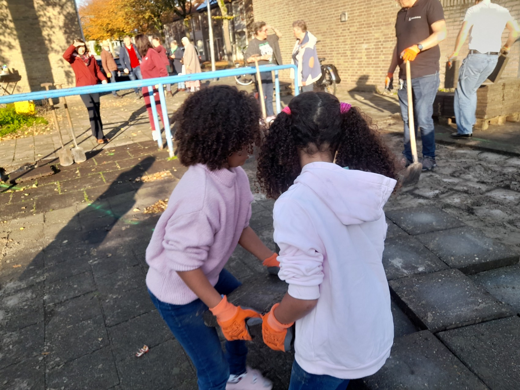 Kinderen helpen bij buitenproject met volwassenen, verplaatsen stenen op een zonnige dag.