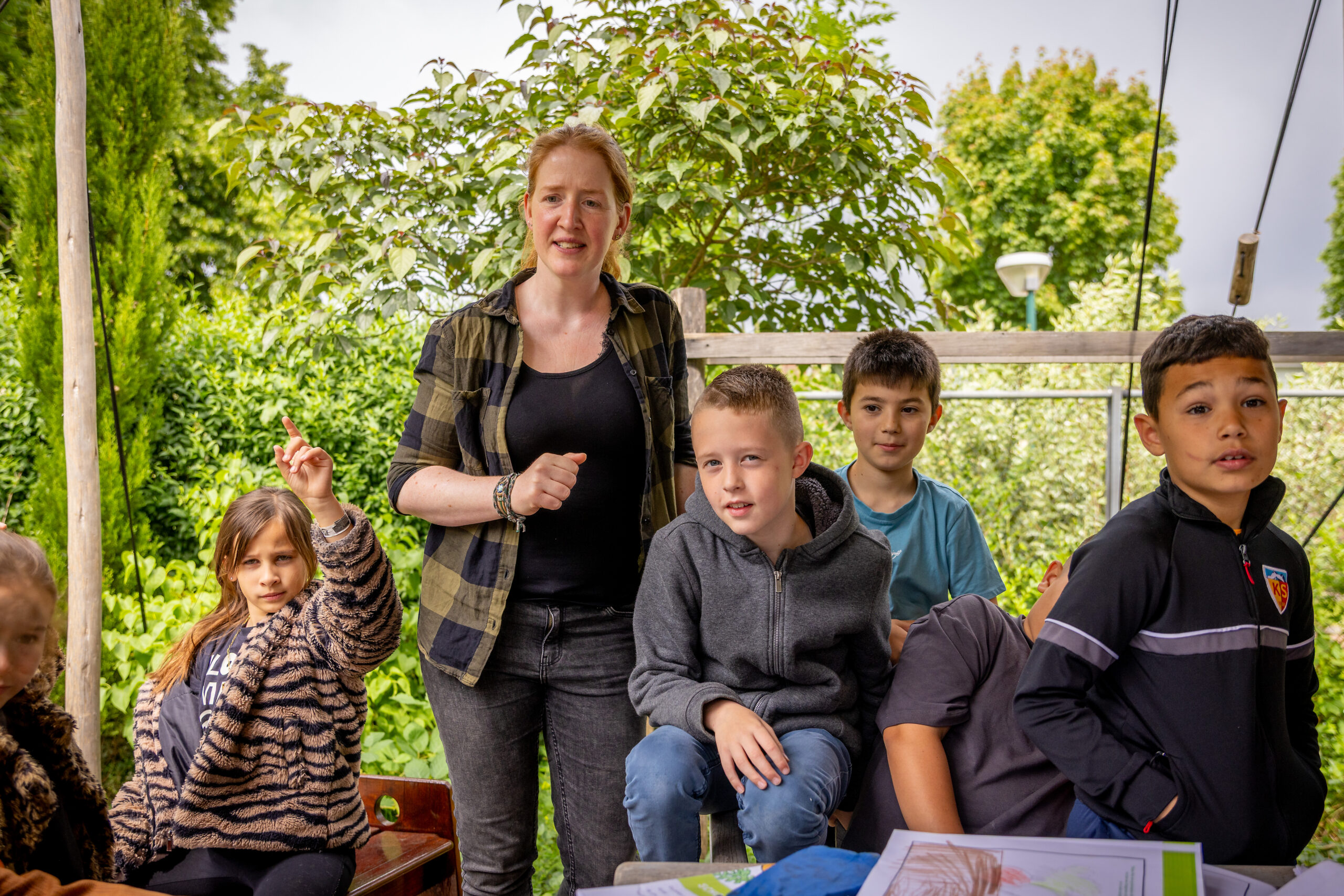 Een vrouw met kinderen in een tuinomgeving, één kind steekt zijn vinger op.