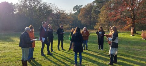 Een groep mensen staat buiten in een kring, omringd door bomen.