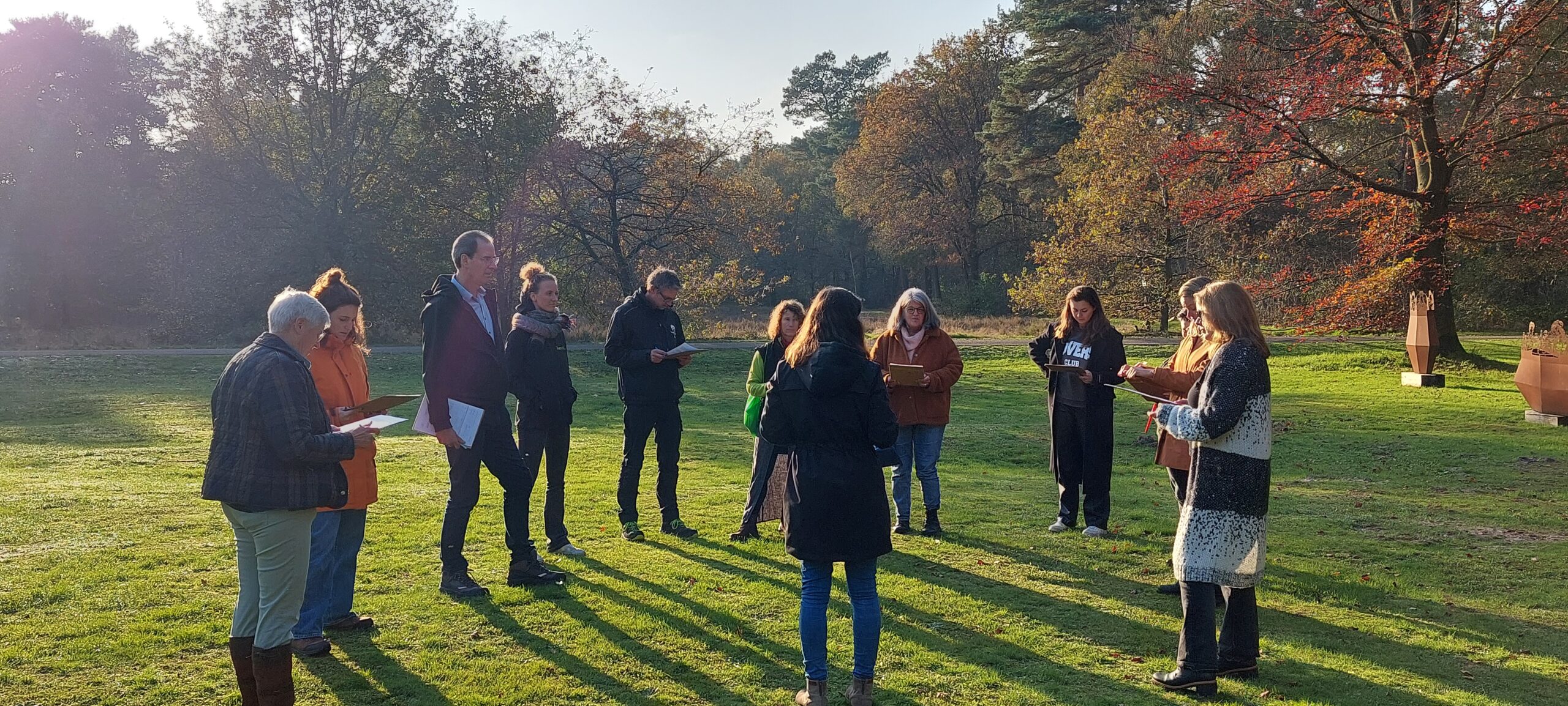 Een groep mensen staat buiten in een kring, omringd door bomen.