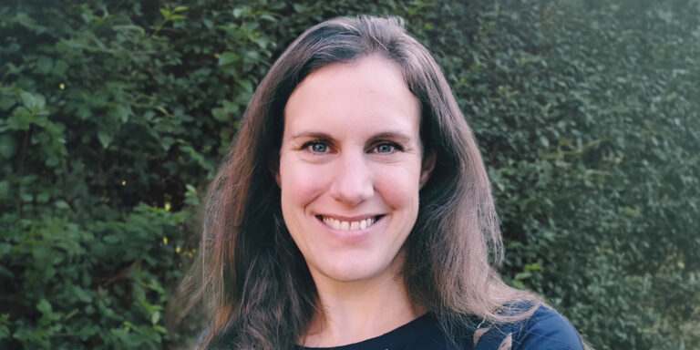 Vrouw met lang haar glimlacht voor een groene achtergrond.