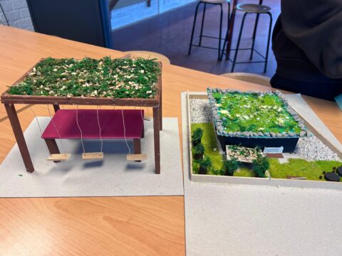Miniatuurbouwprojecten met groene daken en miniatuurschommels op een houten tafel.