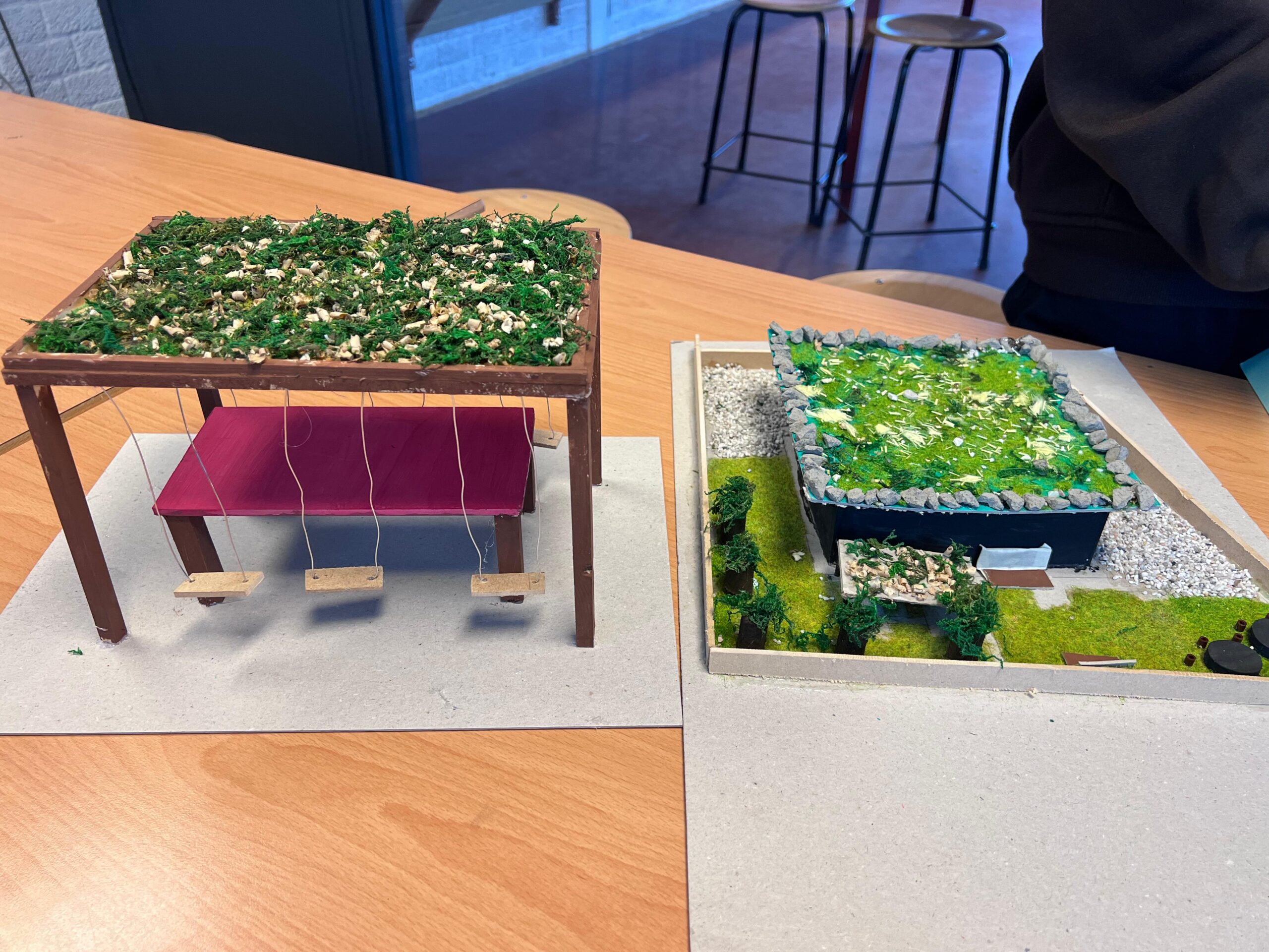 Miniatuurbouwprojecten met groene daken en miniatuurschommels op een houten tafel.