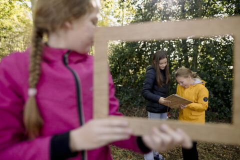 Drie kinderen buiten; een in roze houdt een frame vast, de andere twee kijken naar een plank.