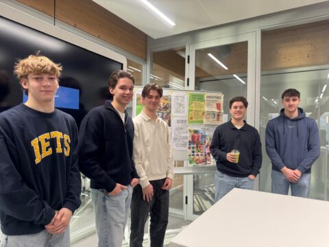 Vijf jongens poseren voor een presentatiebord met informatie over smoothies en soep.