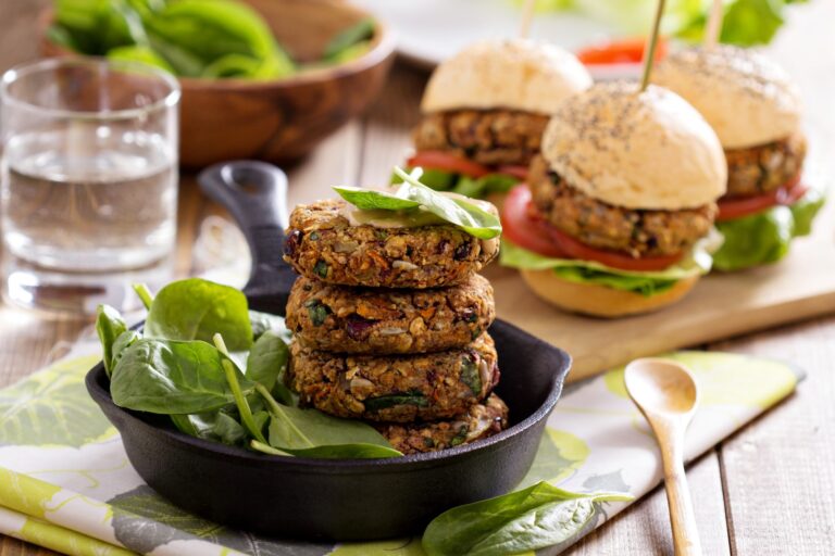 Vegetarische burgers op een bord met spinazie, naast mini burgers op een houten plank.