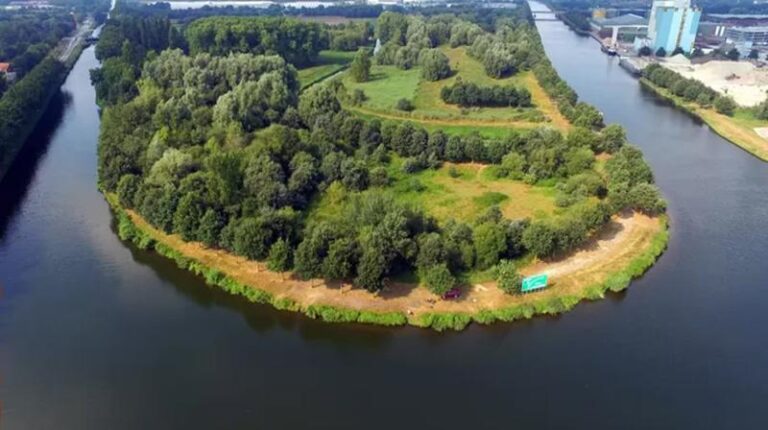 Een groen schiereiland met bomen en gras, omringd door water.