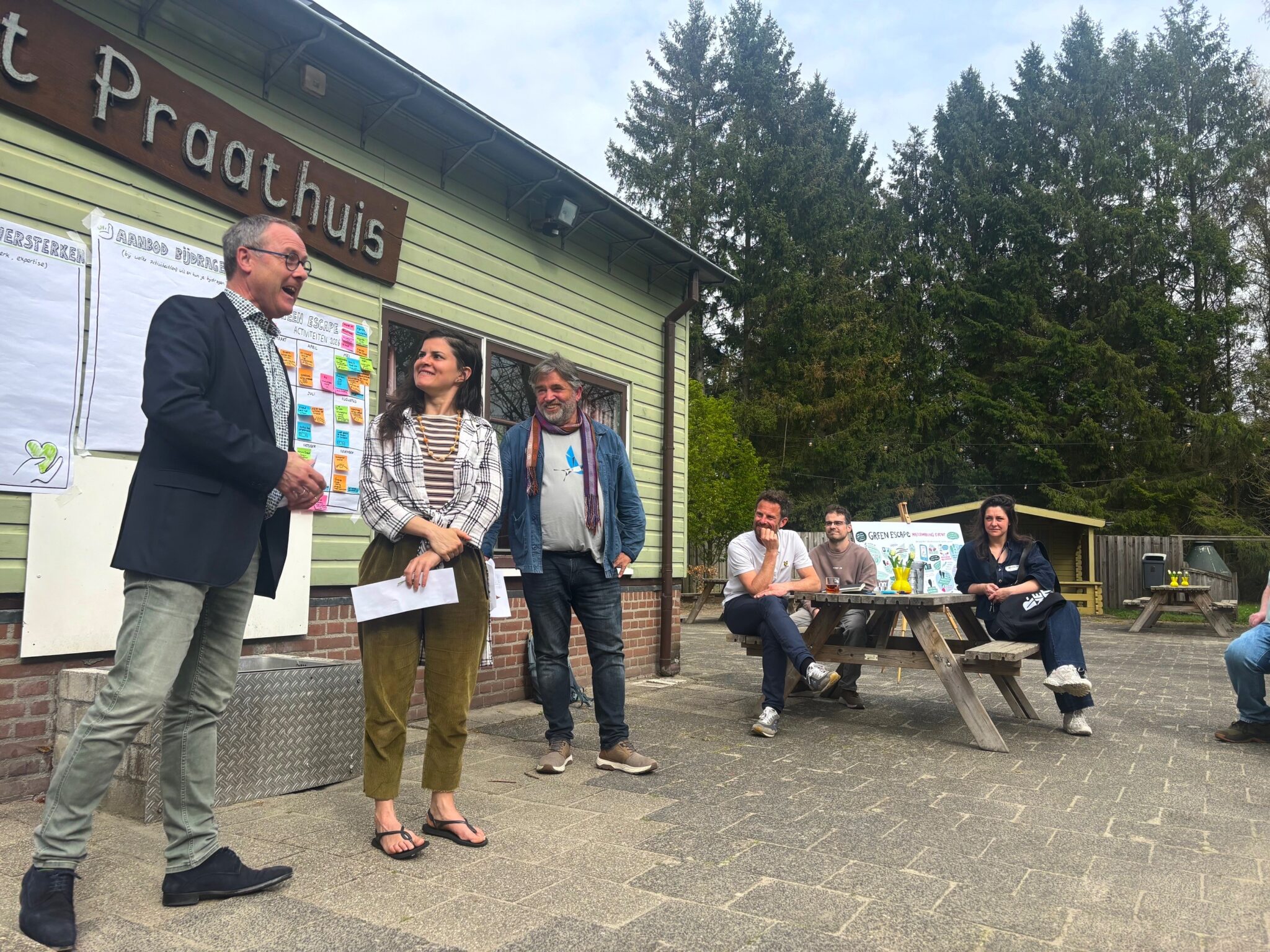 Mensen houden een bijeenkomst buiten bij het 't Praathuis met notities op borden.