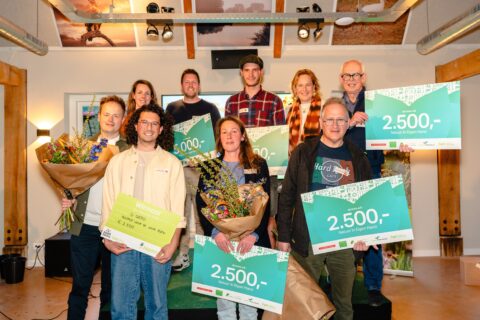 Groep mensen poseert met bloemen en cheques voor een prijsuitreiking, blije gezichten en vreugde.